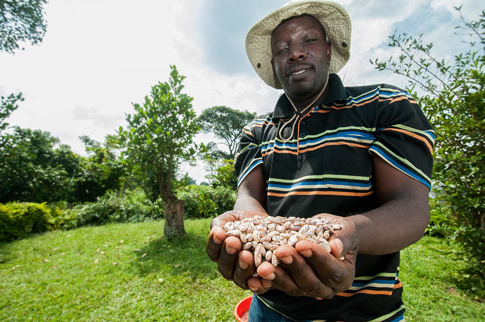 A man standing outdoors holding out his hands, with his hands full of beans